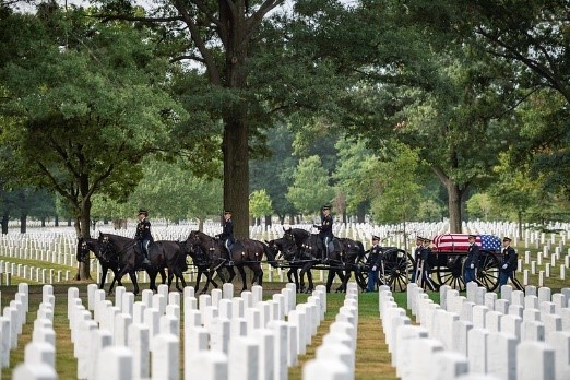 Soldiers on horses pulling a wagon with a casket on top through Arlington cemetery