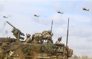 Military vehicle with helicopters flying in the background