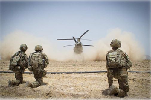 Soldiers kneeling with a chinook landing in the background