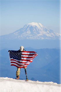 Moutain climber with prostetic leg holding American Flag on top of a mountain