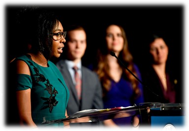 woman giving a speech on stage with others behind her